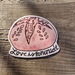 May include: A pink and white sticker with a hand-drawn illustration of a loaf of bread. The text "Love is Homemade" is written below the bread.
