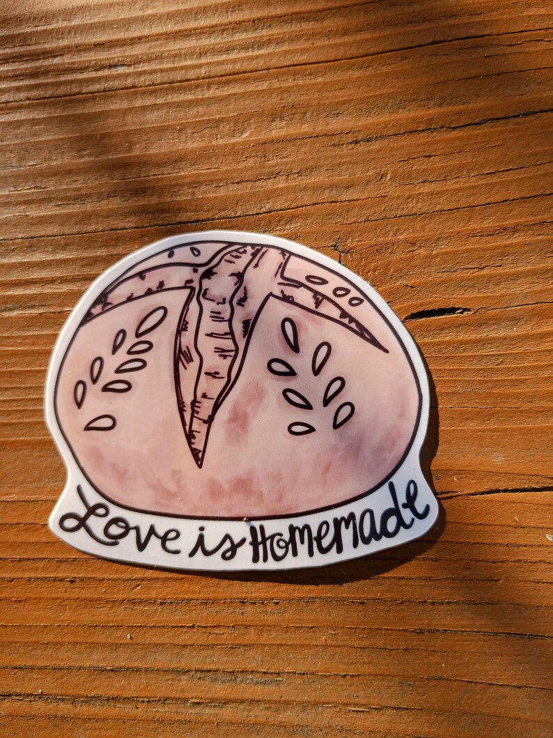 May include: A pink and white sticker with a hand-drawn illustration of a loaf of bread. The text "Love is Homemade" is written in black cursive below the bread.