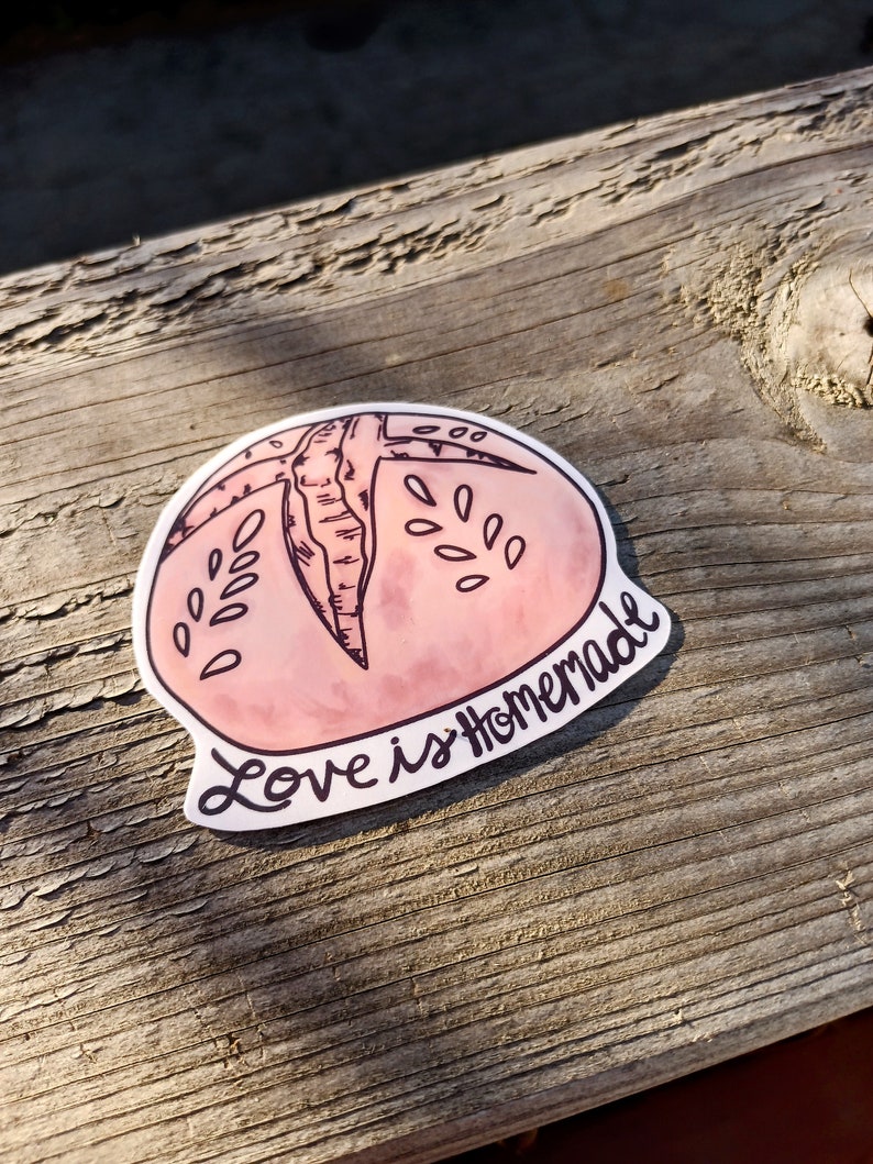 May include: A pink and white sticker with a hand-drawn illustration of a round bread loaf. The text "Love is Homemade" is written in black cursive.
