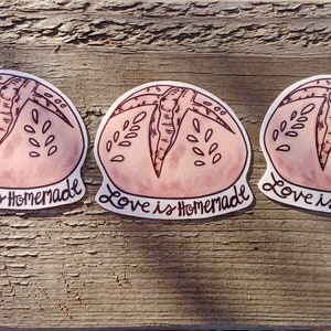 May include: Three pink and white round stickers with a hand-drawn illustration of a loaf of bread. The text "Love is Homemade" is written below each bread illustration.