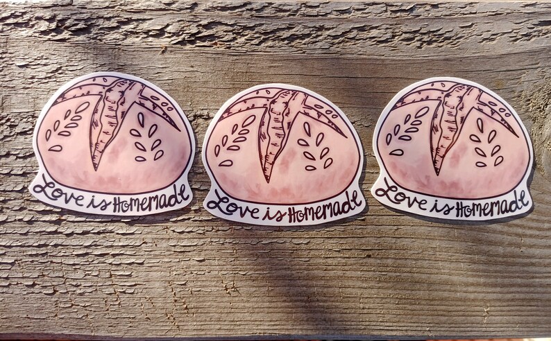 May include: Three pink and white round stickers with a hand-drawn illustration of a loaf of bread. The text "Love is Homemade" is written below each bread illustration.