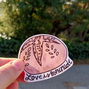 May include: A pink and white sticker with a hand-drawn illustration of a peach and the text "Love is Homemade".