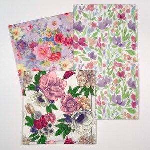 May include: Three floral patterned paper napkins. One napkin features a variety of pink, red, and purple flowers on a lavender background. Another has a white background with pink and purple flowers. The third has a white background with pink, purple, and green flowers.