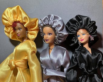 May include: Three dolls wearing satin bonnets in yellow, silver, and black. The dolls are wearing matching satin robes.