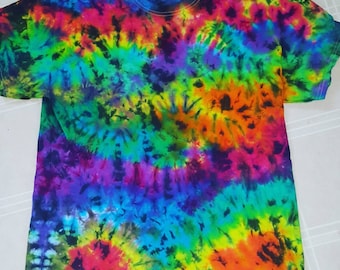 May include: A tie-dye t-shirt with a rainbow swirl pattern in shades of blue, green, yellow, orange, red, and purple. The shirt has a black background with white stitching.