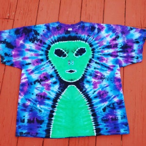Puede incluir: Una camiseta tie-dye con un dise&ntilde;o de cara de extraterrestre verde. La camiseta es una mezcla de azul, morado y negro.