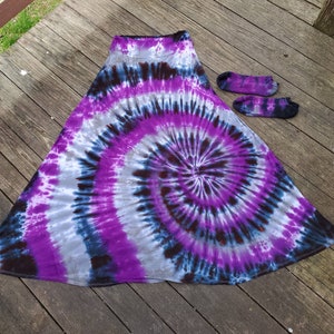 Puede incluir: Una falda larga y fluida con un patrón de tie-dye morado, negro y blanco. La falda está hecha de una tela suave y cómoda y tiene un ajuste holgado.