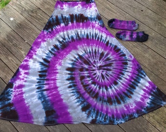 Può includere: Una lunga gonna fluida con un motivo tie-dye viola, nero e bianco. La gonna è realizzata in un tessuto morbido e confortevole e ha una vestibilità rilassata.