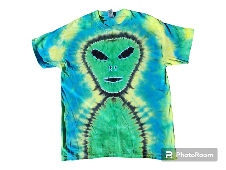 Puede incluir: Una camiseta tie-dye con un dise&ntilde;o de cara de extraterrestre verde. La camiseta es una mezcla de colores azul, verde y amarillo.