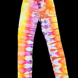Puede incluir: Un par de pantalones vaqueros ajustados con un patrón de tie-dye en tonos de amarillo, naranja, rosa y morado.