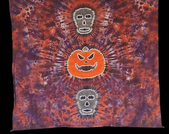 Può includere: Un arazzo da parete in tessuto tie-dye con una zucca e due teschi al centro. Il tessuto è un mix di arancione, viola e bianco.