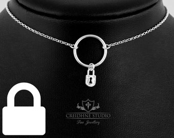 Puede incluir: Un collar de plata con un colgante circular y un pequeño dije de candado. El collar está en un expositor negro. El texto "CREIDHNE STUDIO Fine Jewellery" es visible debajo del collar.