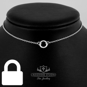 Peut inclure: Un collier en chaîne argent avec un petit pendentif rond. Le collier est sur un présentoir noir.