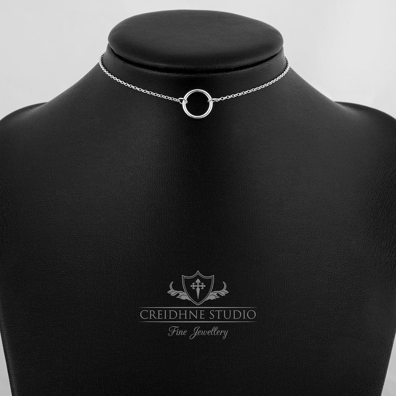 May include: A silver choker necklace with a simple circle pendant. The necklace is displayed on a black mannequin bust. The text "CREIDHNE STUDIO Fine Jewellery" is visible at the bottom of the image.