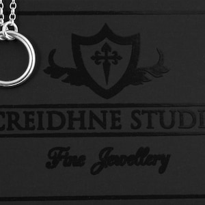 May include: A silver necklace with a double ring pendant on a black background with the text "CREIDHNE STUDIO Fine Jewellery".