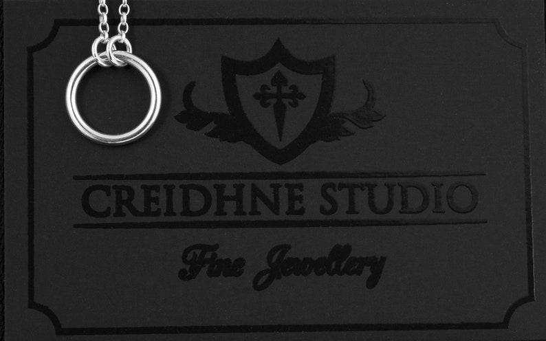 May include: A silver necklace with a double ring pendant on a black background with the text "CREIDHNE STUDIO Fine Jewellery".