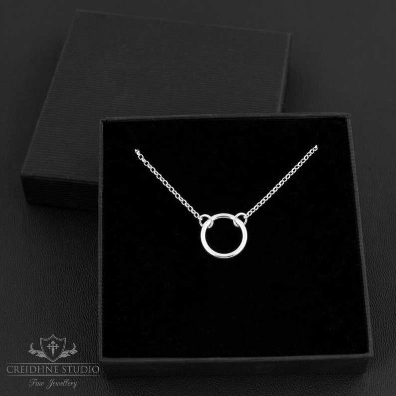 May include: A silver necklace with a simple circle pendant. The necklace is displayed in a black velvet box.