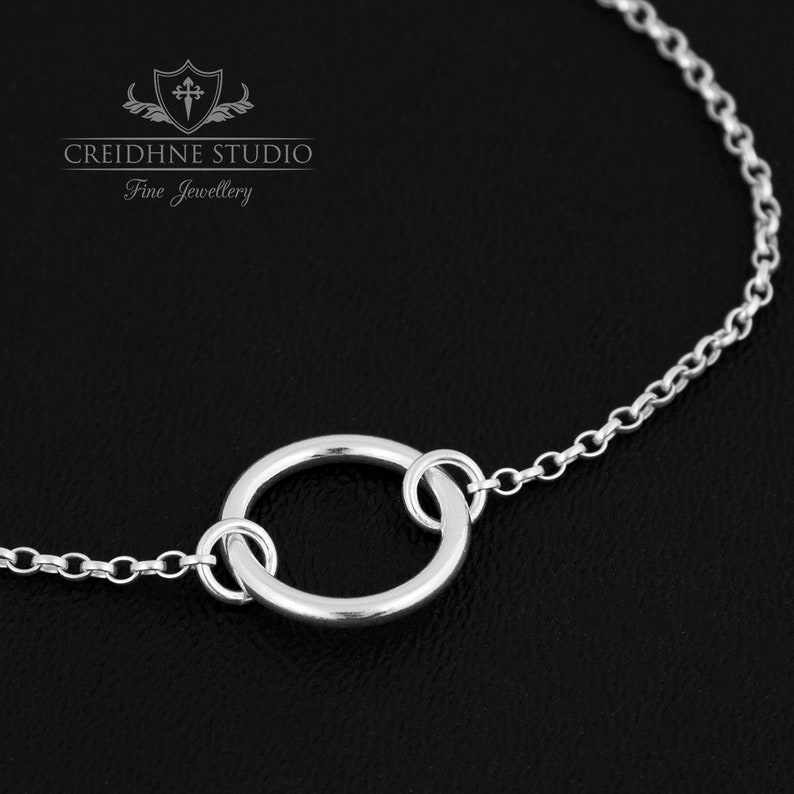 May include: A silver chain bracelet with a simple circle pendant. The chain is delicate and the circle is smooth and polished.