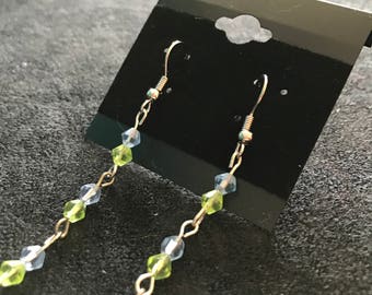 Puede incluir: Un par de pendientes colgantes con una cadena plateada y cuentas facetadas de color azul claro y verde alternadas.