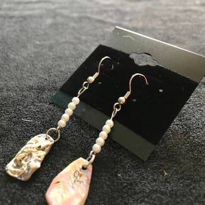 Pode incluir: Um par de brincos de prata com contas de pérolas brancas e pingentes de concha iridescente.