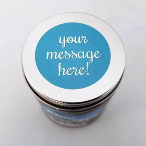 A silver lid with a blue circle in the center. The circle has white text that reads 'your message here!'