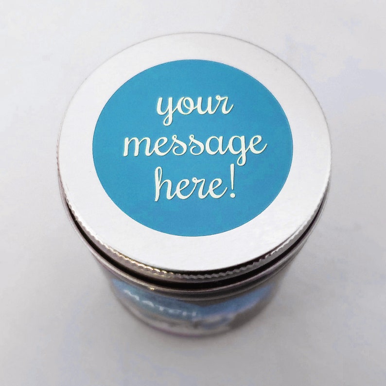 A silver lid with a blue circle in the center. The circle has white text that reads 'your message here!'