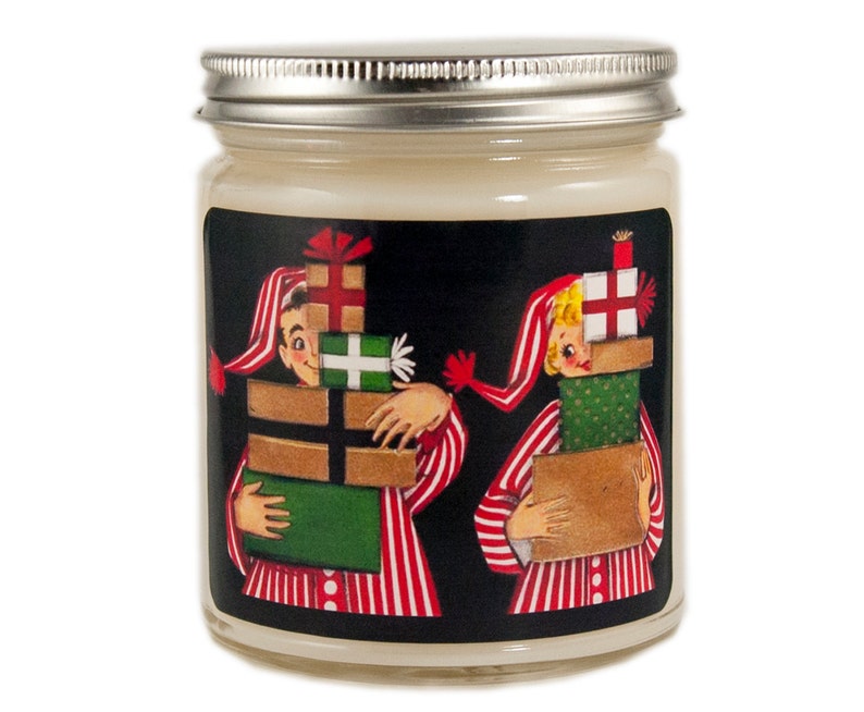K&ouml;nnte beinhalten: Ein Kerzengef&auml;&szlig; mit einer Schwarzwei&szlig;illustration von zwei Personen im Schlafanzug, die Stapel verpackter Geschenke tragen. Der Text auf dem Etikett lautet "Frohe Weihnachten".