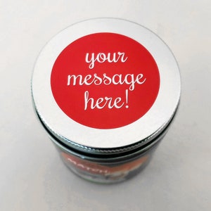 May include: A silver lid with a red circle sticker that says "your message here!" on top of a glass jar.