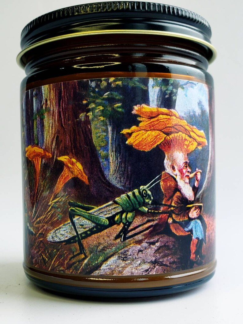 May include: A brown glass jar candle with a colorful label depicting a whimsical scene of a gnome sitting under a mushroom with a grasshopper in the foreground. The label features a forest background with trees and other mushrooms.