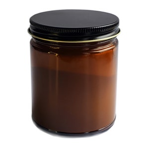 May include: A brown glass candle jar with a black metal lid. The jar is filled with a creamy white candle wax.