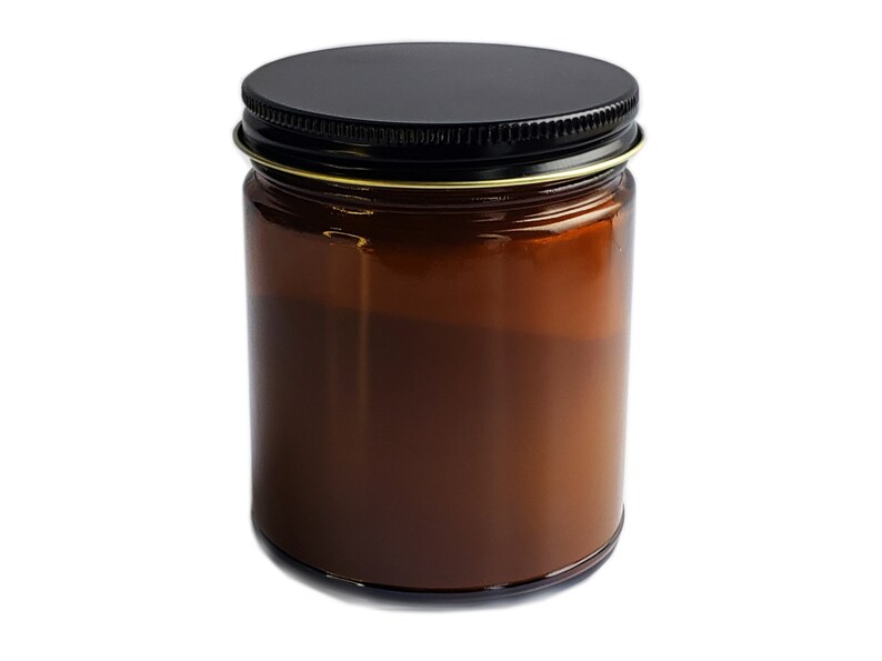 May include: A brown glass candle jar with a black metal lid. The jar is filled with a creamy white candle wax.