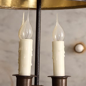 Könnte beinhalten: Ein Kronleuchter mit zwei aufrechten kerzenförmigen Glühbirnen mit klaren Glasflammen, die in cremefarbene Kunststoffhülsen mit realistischen Wachstropfen eingesetzt sind. Die Leuchtmittel sitzen auf dunklen Metallsockeln an einer schwarzen Stange.