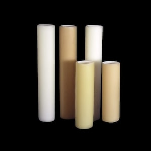 May include: Five cylindrical candles in various shades of beige, cream, and white. The candles are arranged in a row from left to right, with the tallest candle on the left and the shortest candle on the right.