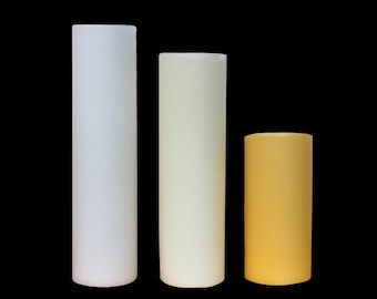 May include: Three pillar candles of varying heights and colors. The tallest candle is white, the middle candle is cream, and the shortest candle is yellow.