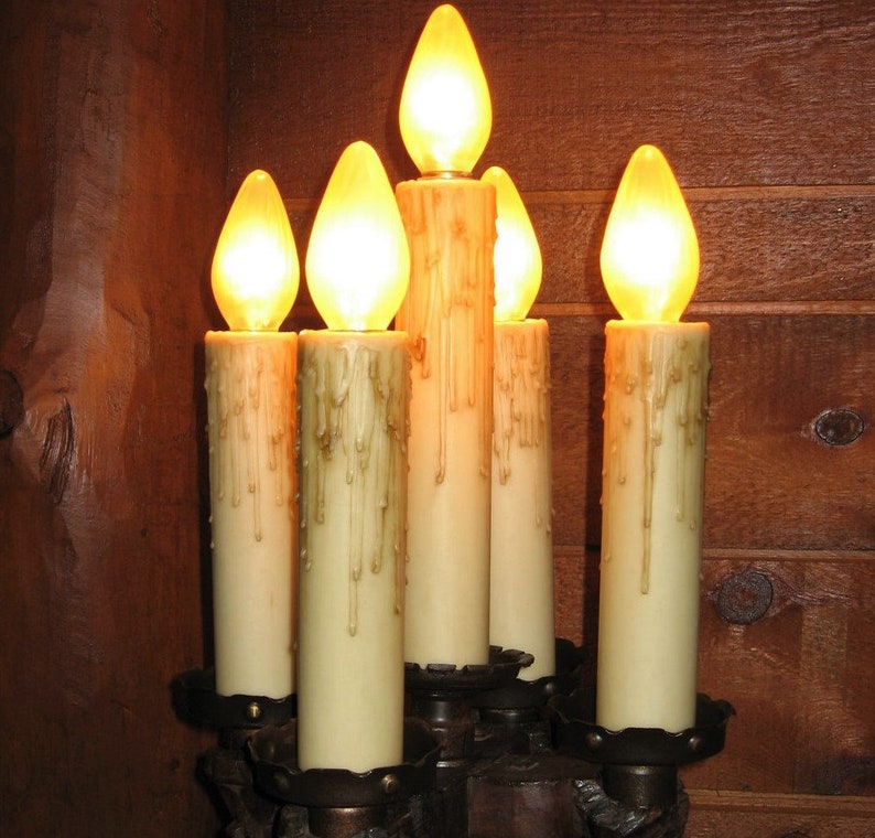 May include: A set of six candle-shaped light bulbs with a warm yellow glow, mounted on a dark brown metal candelabra. The bulbs are arranged in a circular pattern, with the center bulb slightly higher than the others.