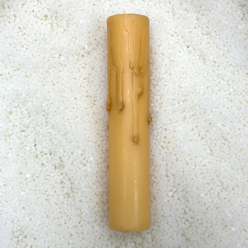 May include: A single, tall, ivory-colored candle with a drip design. The candle is sitting on a white surface.