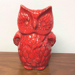May include: A bright red ceramic owl figurine featuring a glossy, crackled glaze finish. The owl has large, circular eyes, a pointed beak, and textured, overlapping feather patterns covering its body, with small wings tucked against its sides.
