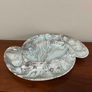 May include: A decorative serving dish with a unique shape and a marbled pattern in shades of gray and light blue. The dish has a central bowl and two side sections, perfect for serving snacks or appetizers.