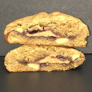 May include: Two halves of a peanut butter and jelly cookie, showing the filling. The cookie is light brown and the filling is a dark red jelly and a white peanut butter.