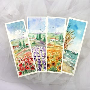 以下が含まれることがあります： 風景画が描かれた4つの水彩画のブックマーク。赤いポピー、ラベンダー、ヒマワリの畑、ヨットのある海岸の風景が描かれています。各ブックマークには白い縁取りと水彩画の空があります。