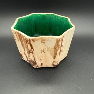 May include: A decorative ceramic bowl with a unique, geometric shape. The exterior features a light beige color with brown streaks, while the interior is a vibrant green. The bowl has a textured appearance and is suitable for various uses.