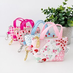 May include: Four miniature fabric tote bags with zip closures and gold-toned lobster clasps. The bags feature various patterns including pink gingham, strawberry prints, blue floral motifs, and patchwork designs with the text Fresh Strawberry.
