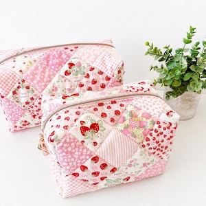 May include: Two rectangular quilted pouches featuring a patchwork design of pink and white fabrics with strawberry patterns, floral prints, and gingham checks. Each pouch has a top zipper closure and a soft, padded construction with visible stitching.