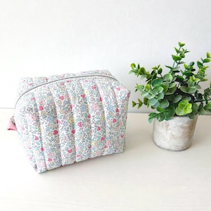 May include: A quilted cosmetic bag with a floral pattern in pink, blue, and yellow on a white background. The bag has a silver zipper and a pink pull tab. The bag is rectangular and appears to be made of fabric.