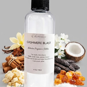 Puede incluir: Una botella de vidrio transparente con tapa negra, etiquetada "CASHMERE BLAST" con notas de fragancia. La imagen incluye vainilla, especias, coco y ámbar, con una capacidad de 118 ml.