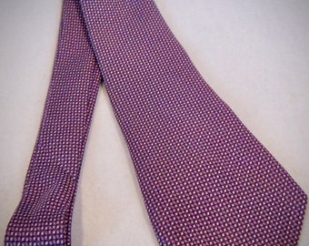 Puede incluir: Una corbata de seda con estampado morado y blanco. La corbata tiene un pequeño patrón geométrico repetitivo.
