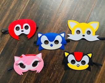 May include: Five felt face masks featuring characters from the Sonic the Hedgehog video game franchise. The masks are blue, red, yellow, pink, and black.