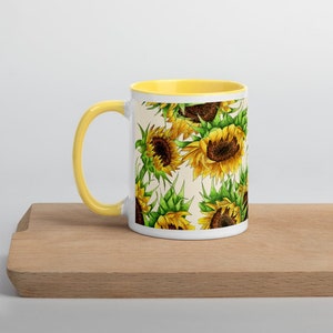 Puede incluir: Taza de cer&aacute;mica blanca con borde amarillo y un patr&oacute;n de girasoles sobre un fondo crema.