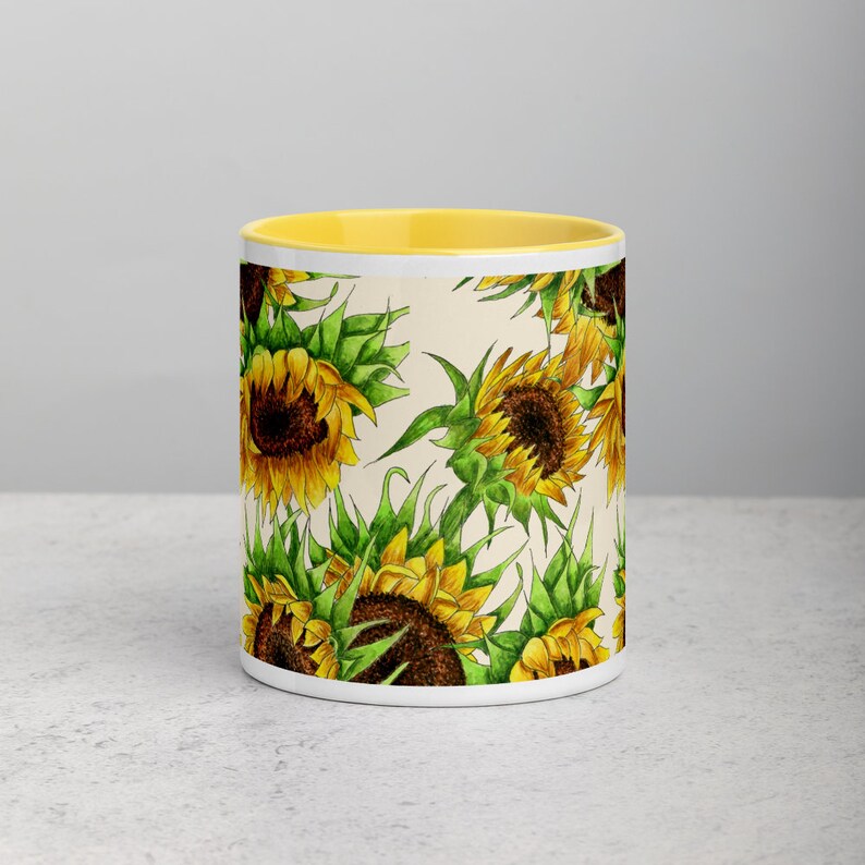 Puede incluir: Taza de cer&aacute;mica blanca con borde amarillo y un patr&oacute;n de girasoles sobre un fondo crema.