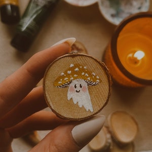 Può includere: Un tondo di legno dipinto a mano con un fungo giallo con puntini bianchi e un viso sorridente bianco.